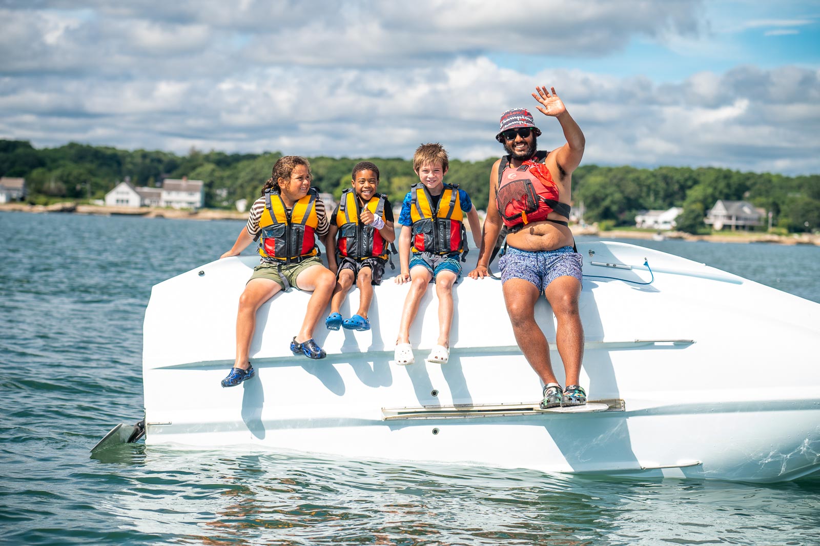 junior sailors and an instructors waving from a capsized boat