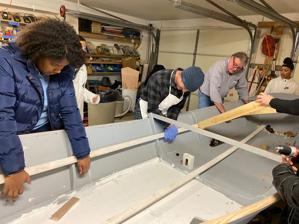 Students and volunteers building a wood rowboat